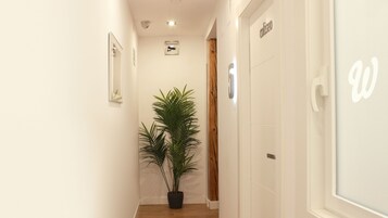 Een smalle gang met een kamerplant, een houten deur en een witte muur met een bord.