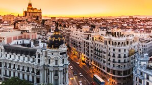 Un edificio histórico con arquitectura ornamentada, una cúpula central y una calle concurrida en primer plano.