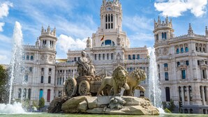 Un edificio imponente con una torre central, una estatua de una figura sentada y una estatua de león al frente.
