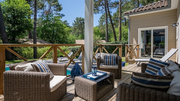 Une terrasse en bois avec des meubles en osier, notamment des canapés et des fauteuils, et une piscine.