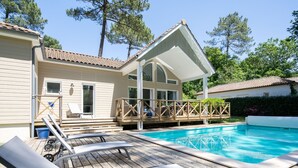 Une terrasse en bois avec une piscine, des chaises longues et un espace patio couvert.