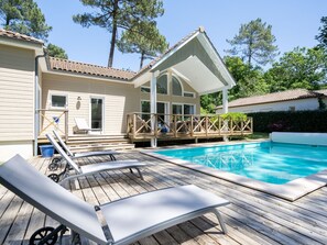 A wooden deck with a pool, lounge chairs, and a covered patio area.