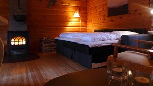 A cozy cabin room with a wooden interior, a bed with white bedding, a table with glasses and a candle, and a wood-burning stove. - Velfjord camping & hytter (Brønnøy)