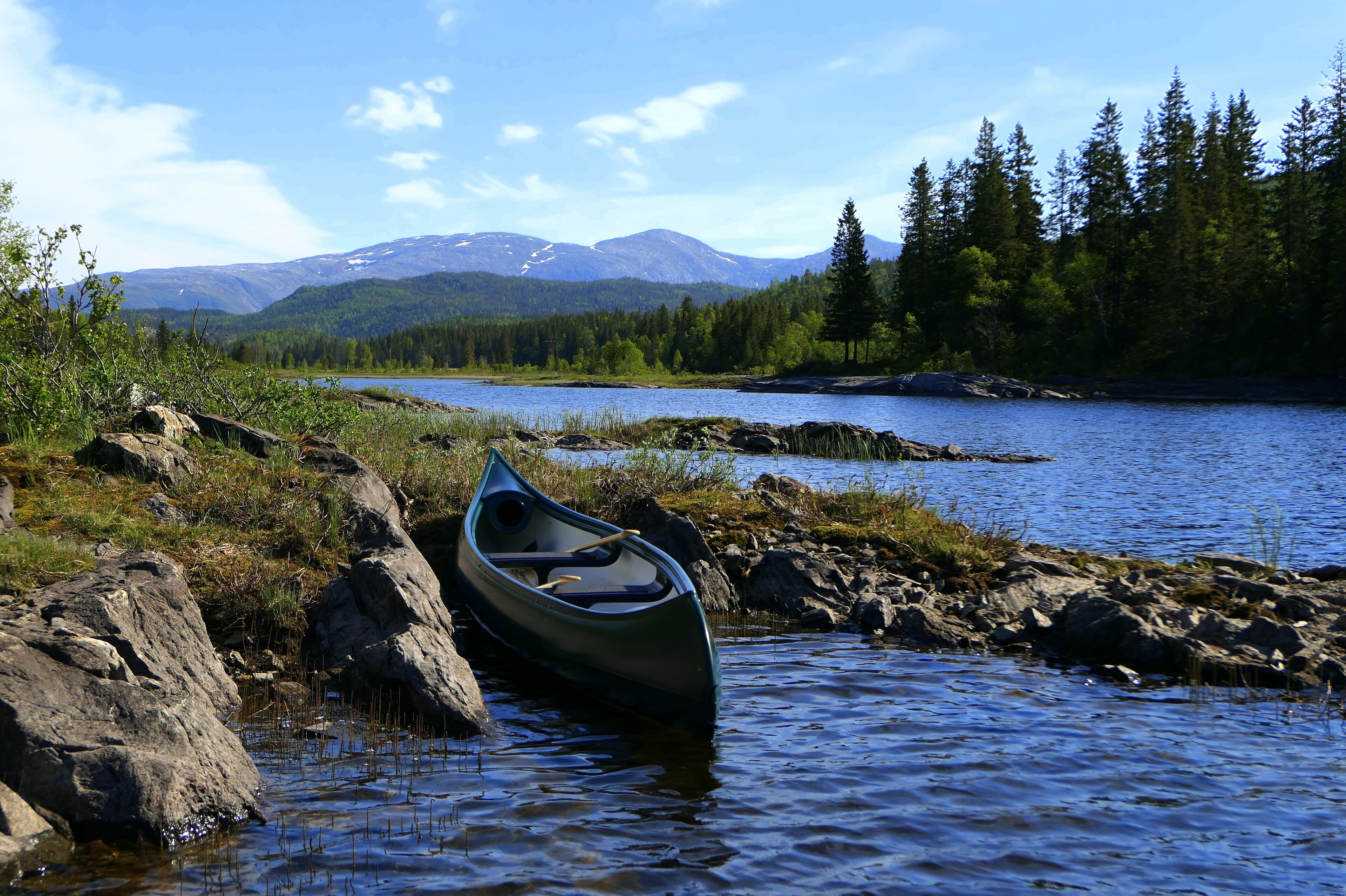 A canoe tied to a rocky shore by a calm lake with mountains in the background.