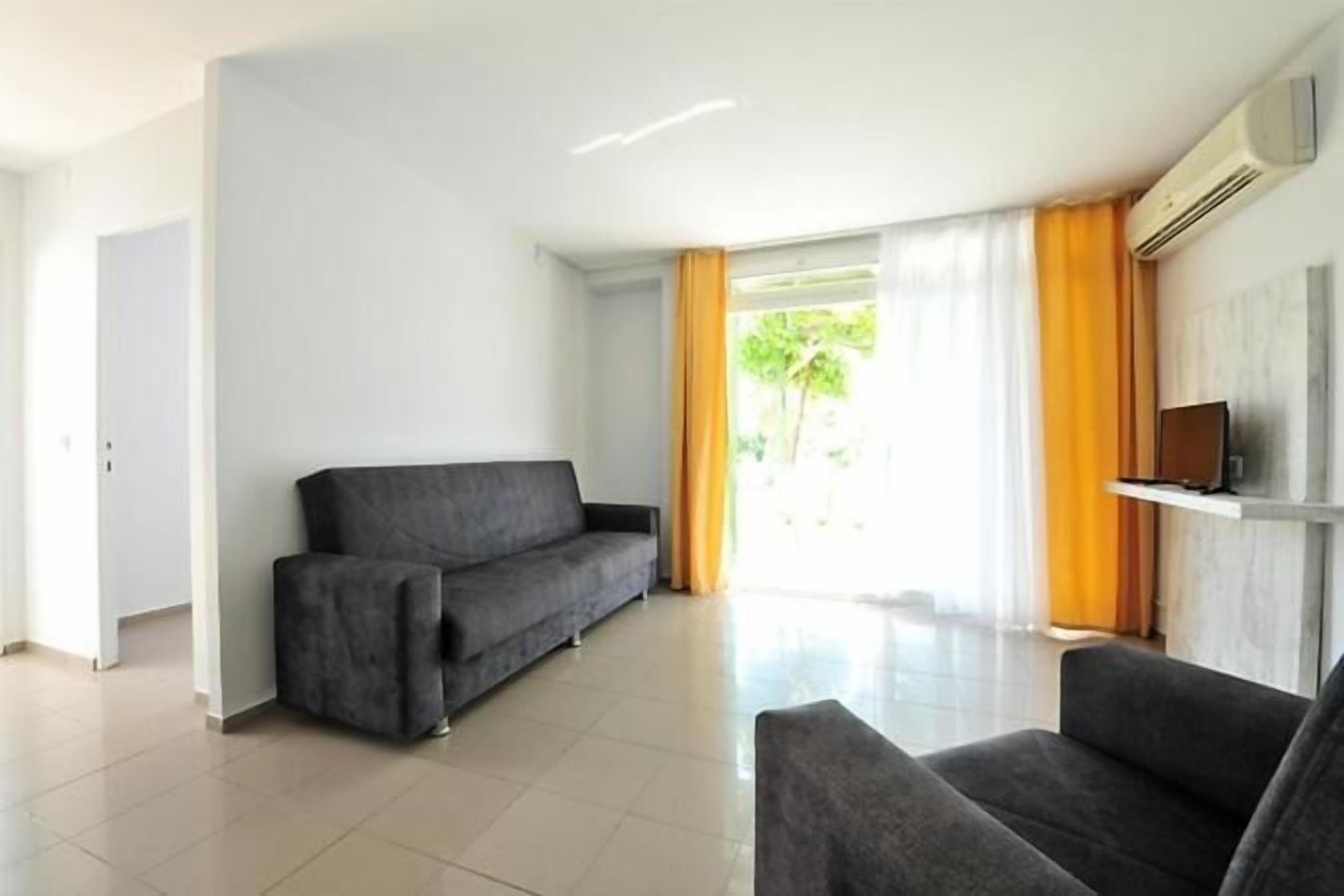 A modern living room with a grey sofa, a smaller armchair, and a flat-screen TV on a white shelf.