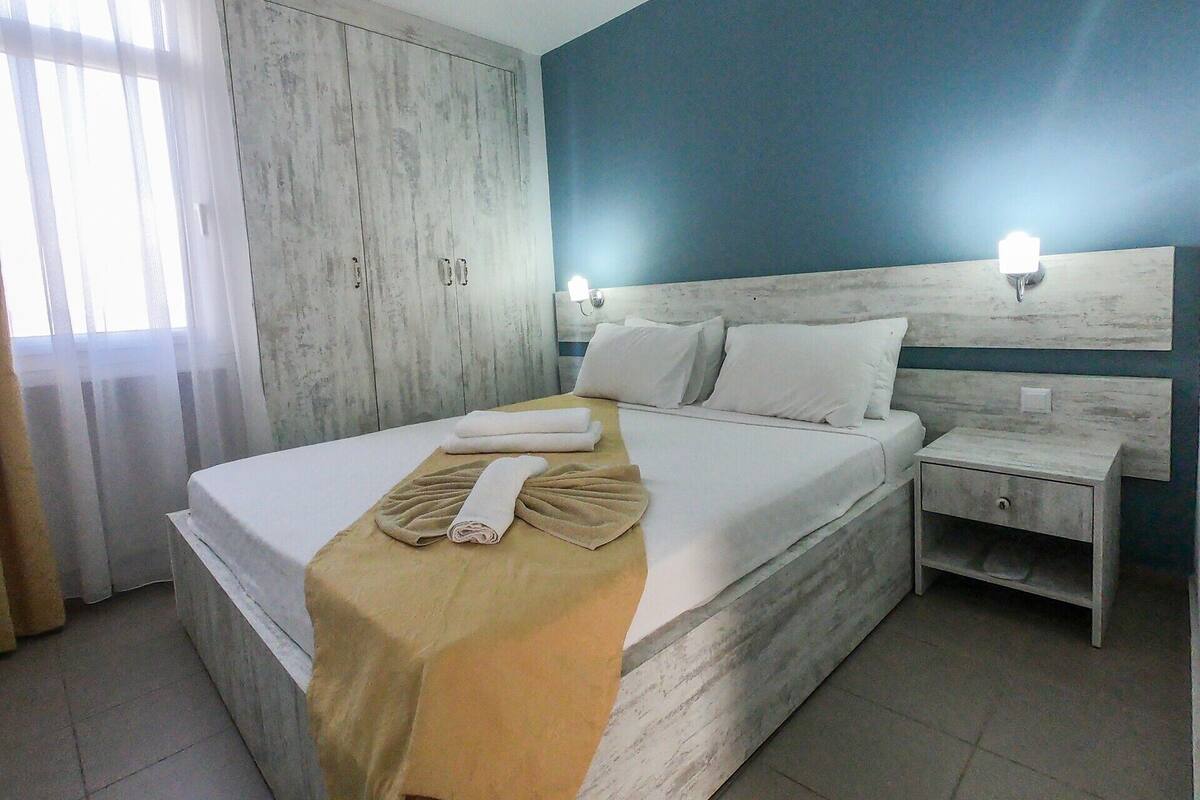 A hotel room with a bed, a nightstand, a wardrobe, and a window with curtains.