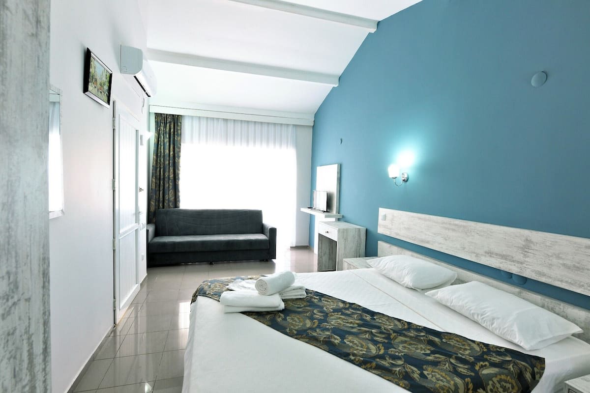 A modern hotel room with a large bed, a sofa, a desk, and a mirror.