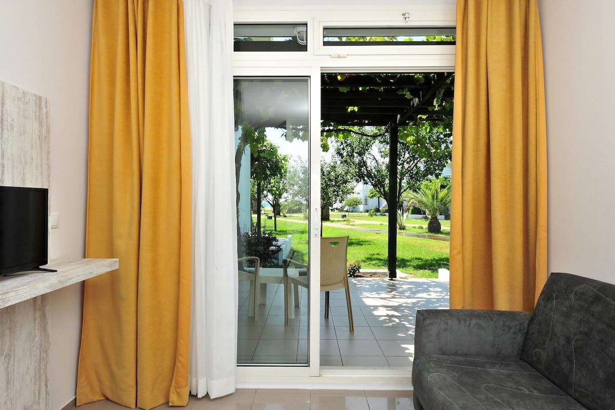 A living room with a sofa, a TV on a shelf, and a sliding glass door leading to an outdoor patio with a table and chairs.