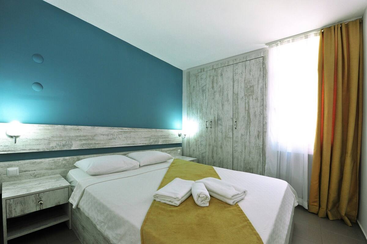 A hotel room with a bed, a nightstand, a wardrobe, and a window with curtains.