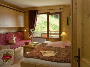 A wooden cabin room with a bed, a bench, a table with a vase, and a window with curtains. - Mountain-style studio for 4 with parking and pets allowed (Le Grand-Bornand)