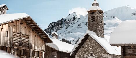 Un edificio de madera rústico con una torre de iglesia de piedra, rodeado de montañas nevadas.