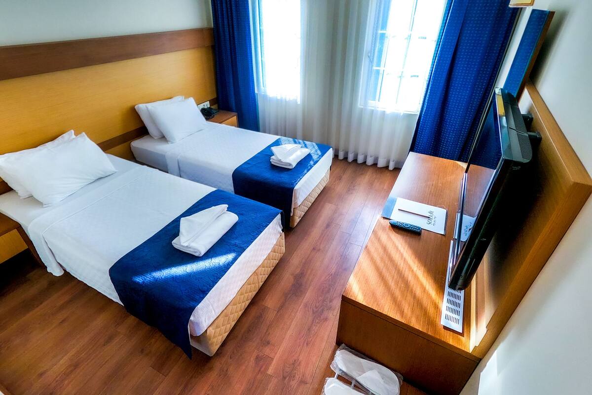 Habitación de hotel con dos camas, piso de madera, un escritorio con teléfono y control remoto, y una ventana con cortinas.