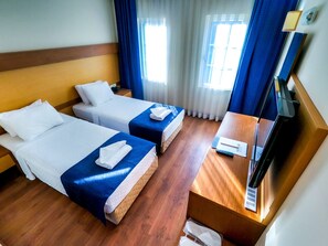 Une chambre d’hôtel avec deux lits, un plancher en bois, un bureau avec un téléphone et une télécommande, et une fenêtre avec des rideaux.