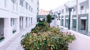 Un pasillo moderno de hotel con paredes blancas, un camino central y abundante vegetación.