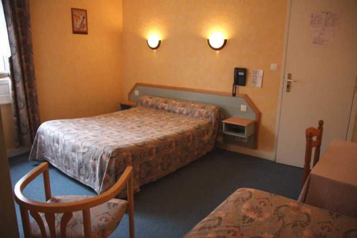A hotel room with a bed, a chair, a desk, and two wall-mounted lights.