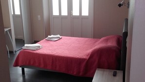 A bedroom with a bed, a bedside table, a window, and a door. - Hotel de la Gare (Dol-de-Bretagne)