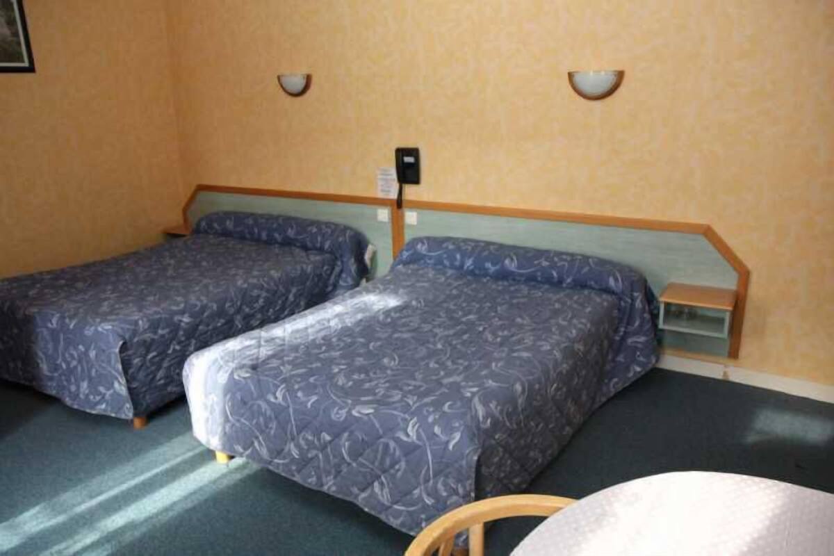 A room with two single beds, a small table, and a wall-mounted light fixture.