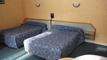 A room with two single beds, a small table, and a wall-mounted light fixture.
