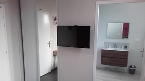A modern bedroom with a large mirror, a flat-screen TV, and a wooden vanity. - Hotel de la Gare (Dol-de-Bretagne)