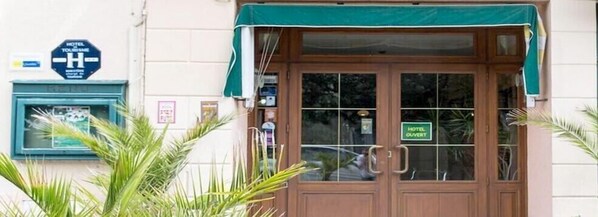 A hotel entrance with a green awning, a sign indicating 'HOTEL TOURISM', and a 'HOTEL OUVERT' sign. - Hotel de la Gare (Dol-de-Bretagne)