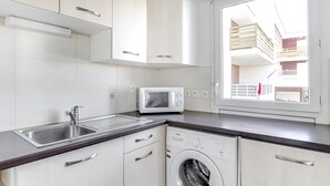 Una cucina moderna con mobili bianchi, un forno a microonde integrato, una lavatrice e una finestra con vista su un balcone.