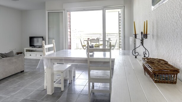 Un soggiorno moderno e minimalista con zona pranzo, televisione e balcone vista.