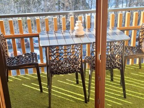 A balcony with a table and chairs, a decorative vase, and a view of a parking lot and trees.