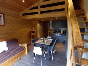 A wooden interior with a dining area, kitchen, and a loft bedroom.