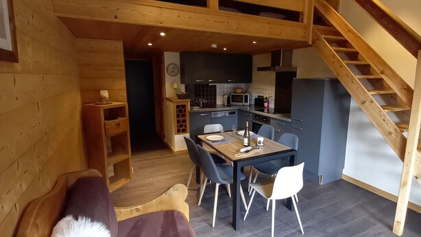 Ein gemütliches Zimmer mit Holzbalkendecke, einem Essbereich mit Tisch und Stühlen, einer Küche mit modernen Geräten und einer Treppe.