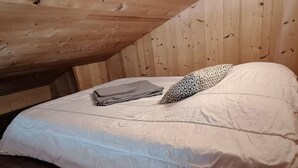 Ein Einzelbett mit weißer Matratze und einem gemusterten Kopfkissen, eine gefaltete Decke und eine Holzbalkendecke.