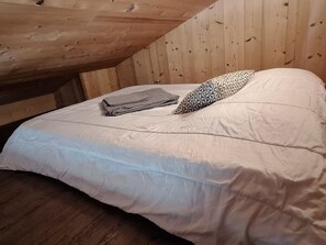 A single bed with a white mattress and a patterned pillow, a folded blanket, and a wooden ceiling. - Cozy apartment 5 pax, near ski slopes, balcony with mountain view (Le Grand-Bornand)