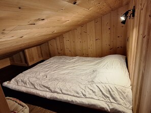 A single bed in a wooden room with sloped ceilings and a small wall-mounted light.