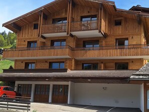 A multi-story wooden building with balconies, a garage, and a parking area. - Cozy apartment 5 pax, near ski slopes, balcony with mountain view (Le Grand-Bornand)