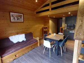 L’intérieur chaleureux d’un chalet avec un canapé en bois, une table à manger avec des chaises, un coin cuisine et un plafond en bois.
