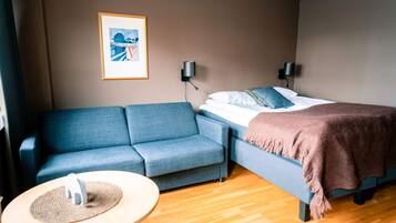 Une chambre d’hôtel moderne, équipée d’un canapé, d’un lit avec une couverture, d’une petite table ronde avec un set de table, et de deux lampes fixées au mur.