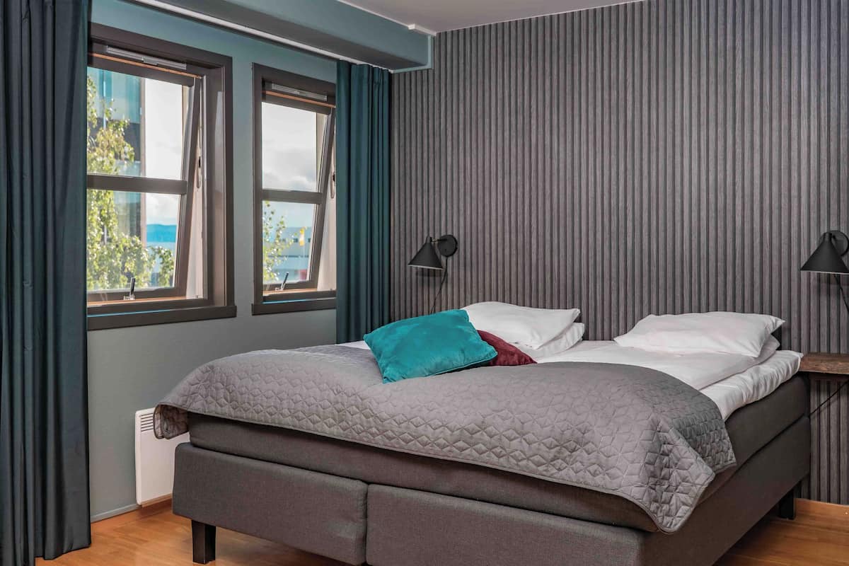 Un dormitorio moderno con cama, dos ventanas y vistas a zonas verdes.