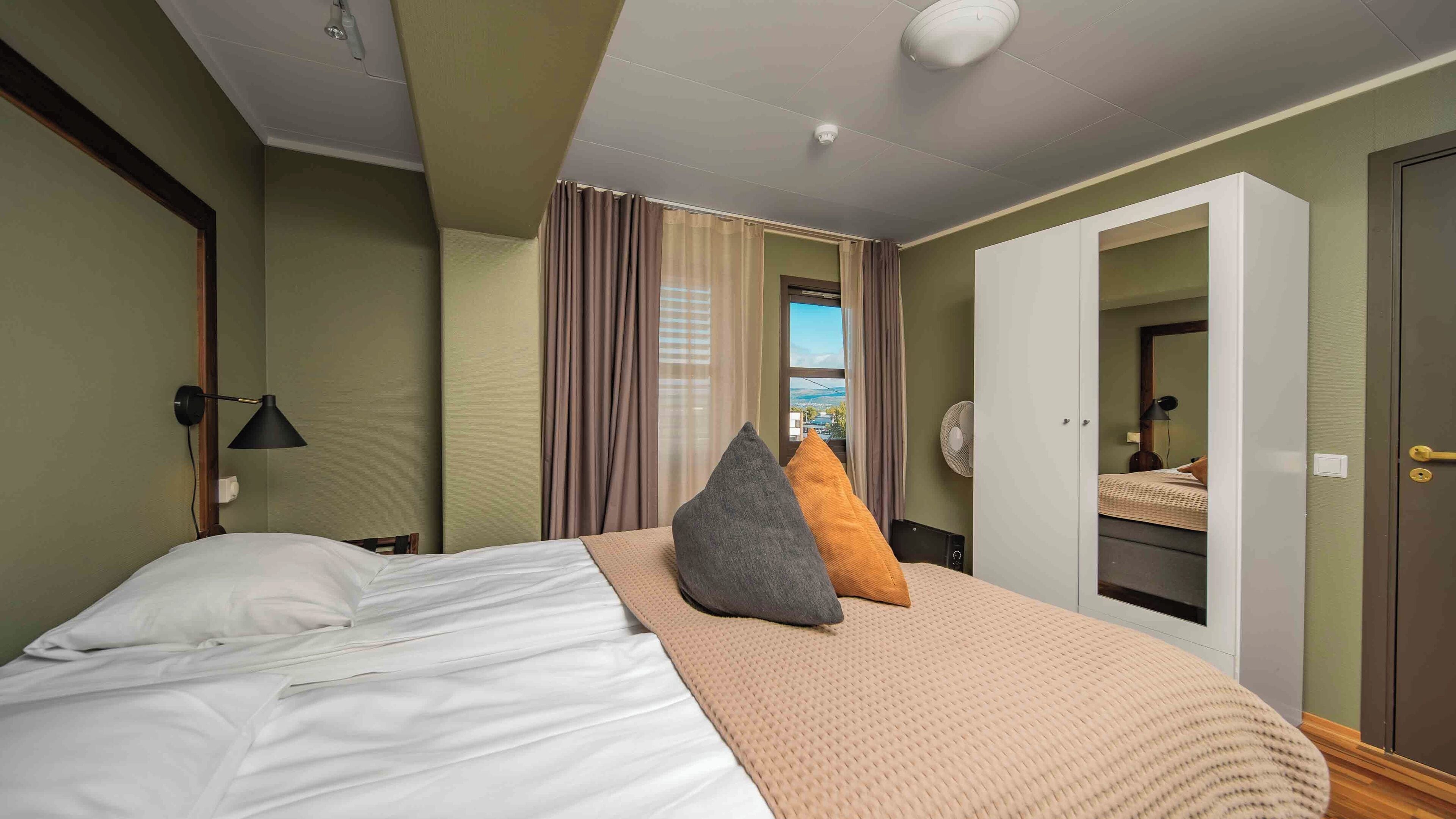 Una habitación de hotel con una cama, una lámpara de noche, una ventana con cortinas, un armario y una puerta.