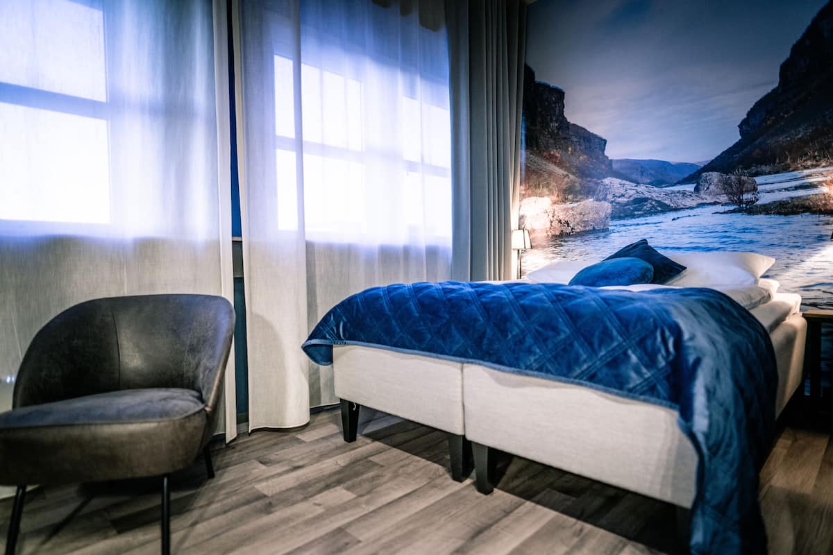 Un dormitorio con cama, una silla y vista a un paisaje nevado a través de una ventana.