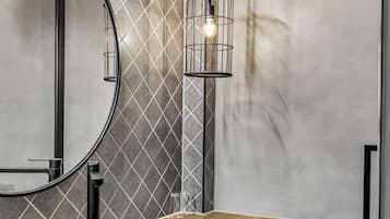 A modern bathroom with a round mirror, a black vessel sink on a wooden countertop, and a hanging light fixture.