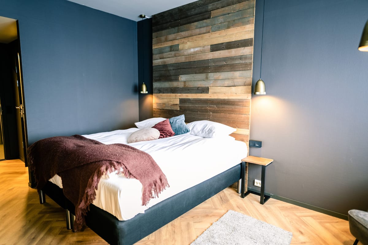 Un dormitorio moderno con cabecera de madera, cama con ropa blanca y dos lámparas de noche.