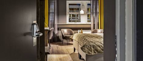 A hotel room with a bed, a desk, a chair, a telephone, and a window with curtains.