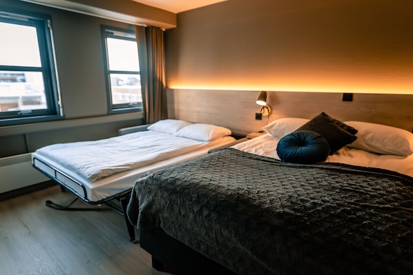 A hotel room with two beds, a window, and a wall-mounted lamp. - Canyon Hotell (Alta)