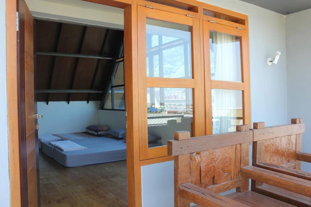 A room with a bed, a wooden bench, and a window with a view of buildings.
