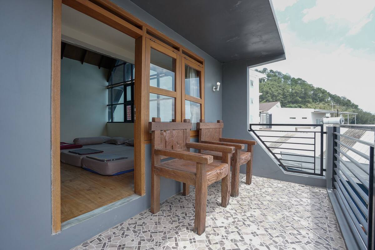 A balcony with a tiled floor, wooden chairs, and a view of a building and trees.