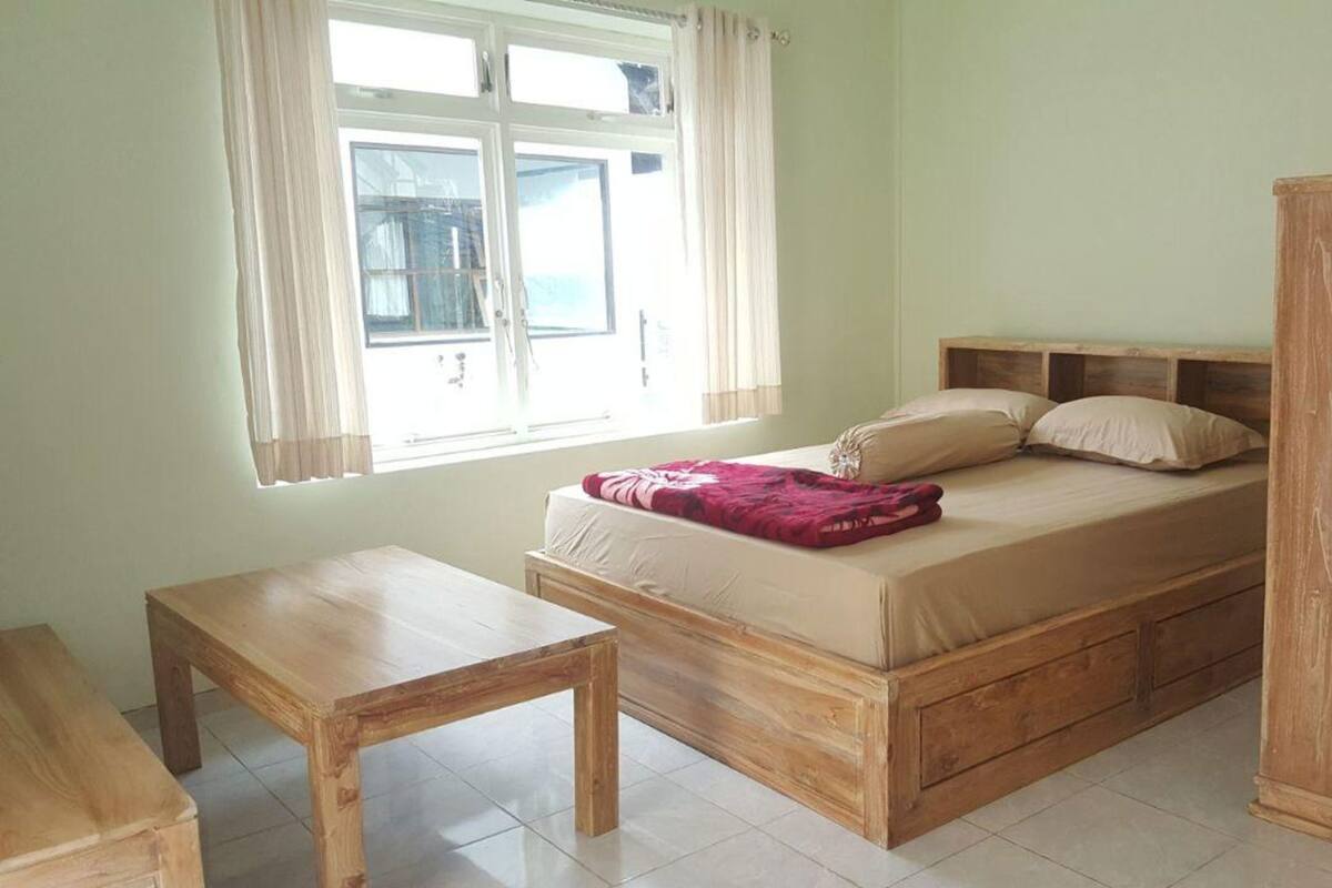 A bedroom with a bed, a wooden nightstand, a wardrobe, and a window with curtains.