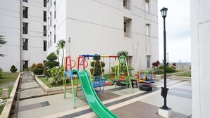Un terrain de jeux avec un toboggan vert et diverses structures de jeu, entouré d’un bâtiment doté de nombreuses fenêtres et d’un lampadaire.