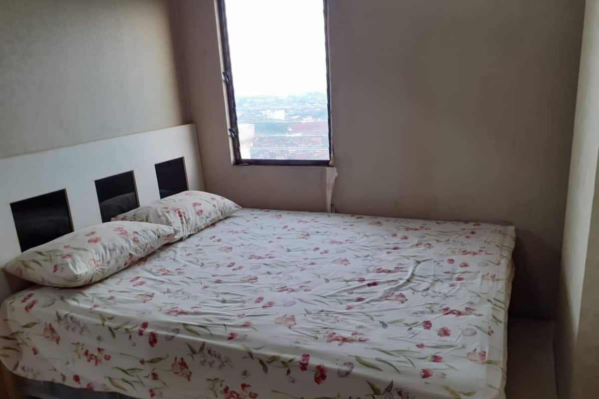 A bedroom with a bed, two pillows, a window, and a view of the city.
