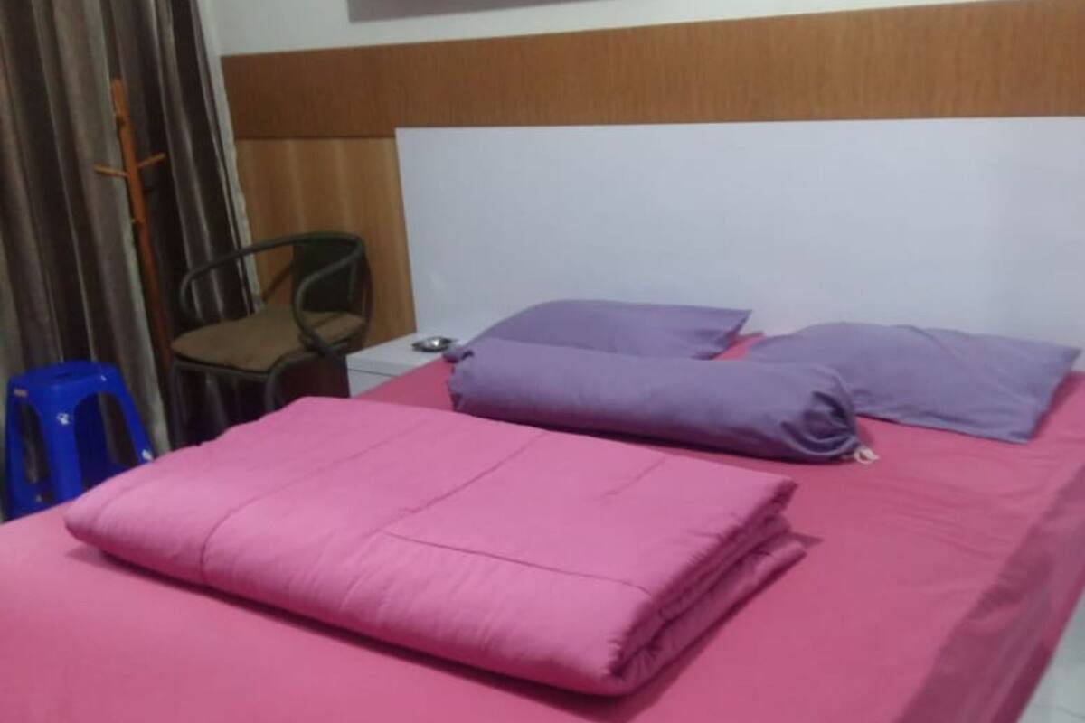 A room with a bed, a nightstand, a chair, and a small wooden shelf.