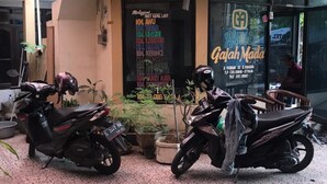 A building with a sign reading "Gajah Mada" and a list of room types. Two motorcycles are parked in front. - Hotel Gajah Mada (Surabaya)