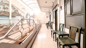 A corridor with a staircase, benches, and a mural on the wall. - Hotel Gajah Mada (Surabaya)